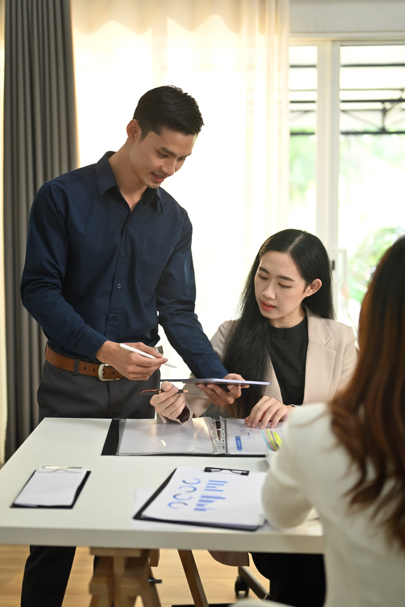Asian male manager discussing financial data on a tablet with a female colleague, demonstrating collaborative outsource financial services.