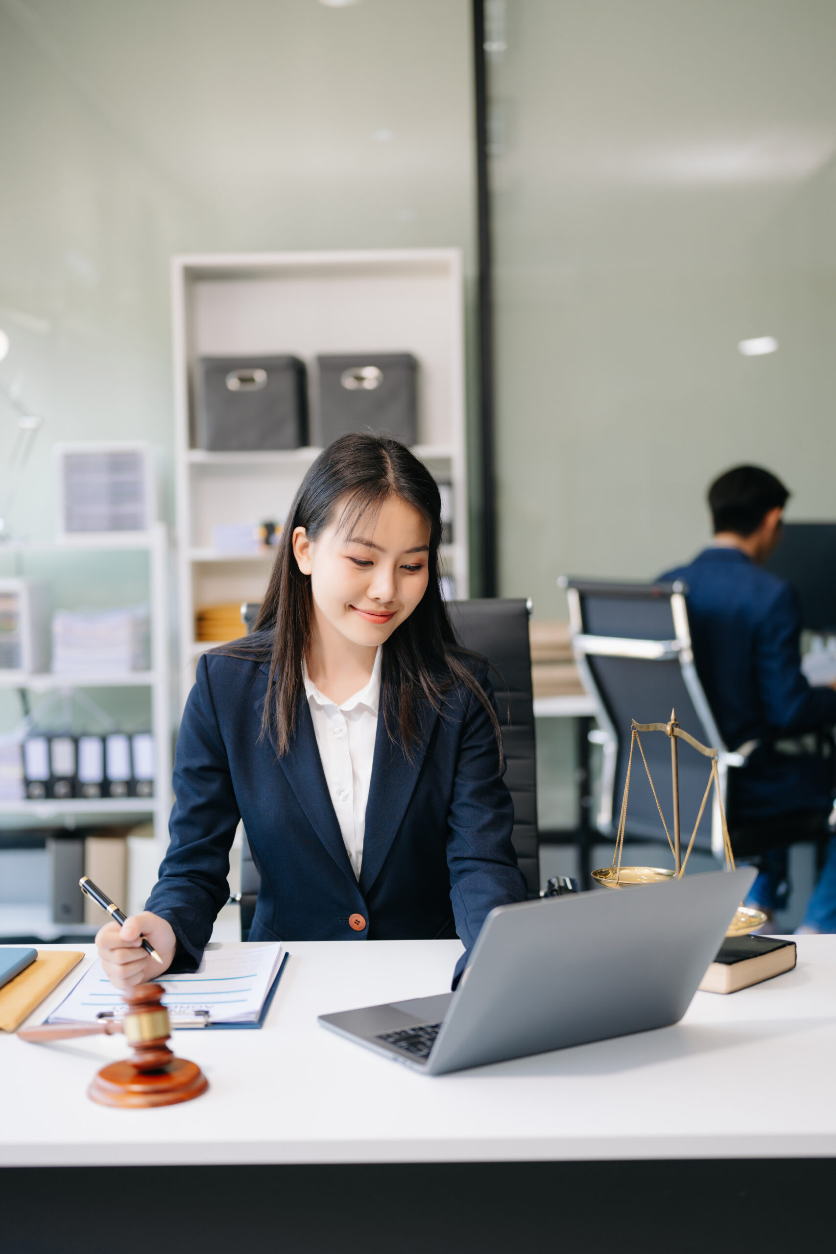 Smiling Asian woman lawyer working on laptop and documents with a gavel nearby, symbolizing efficient legal process outsourcing services.