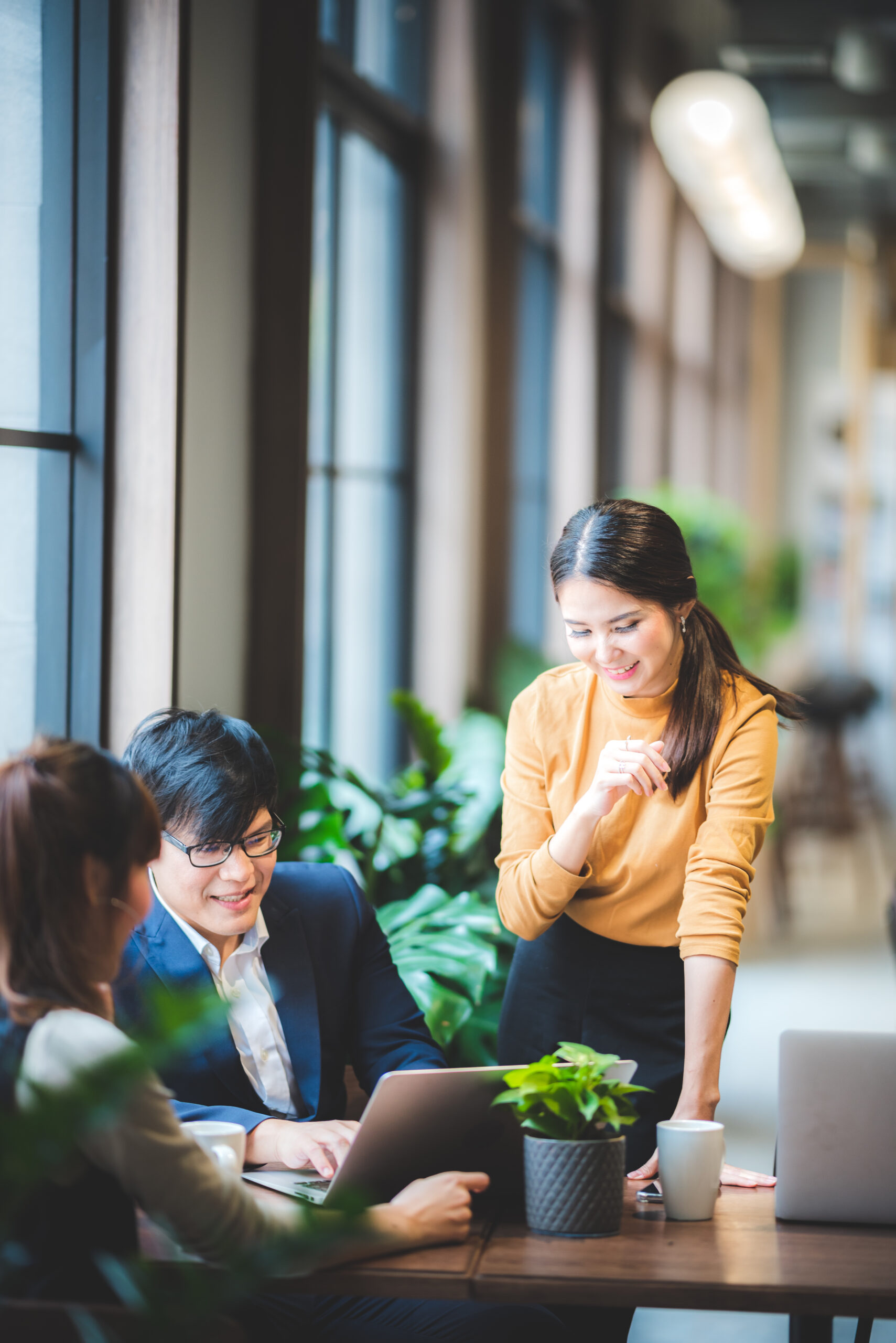A group of smiling Asian business people collaboratively discussing a project with a laptop, reflecting teamwork for effective telemarketing services.