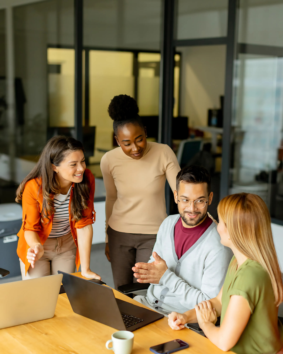 Diverse-Startup-Team-Collaboration-in-Philippine-Outsourcing (1) A young, diverse startup team actively collaborates around laptops in a modern office, engaged in discussion and problem-solving.